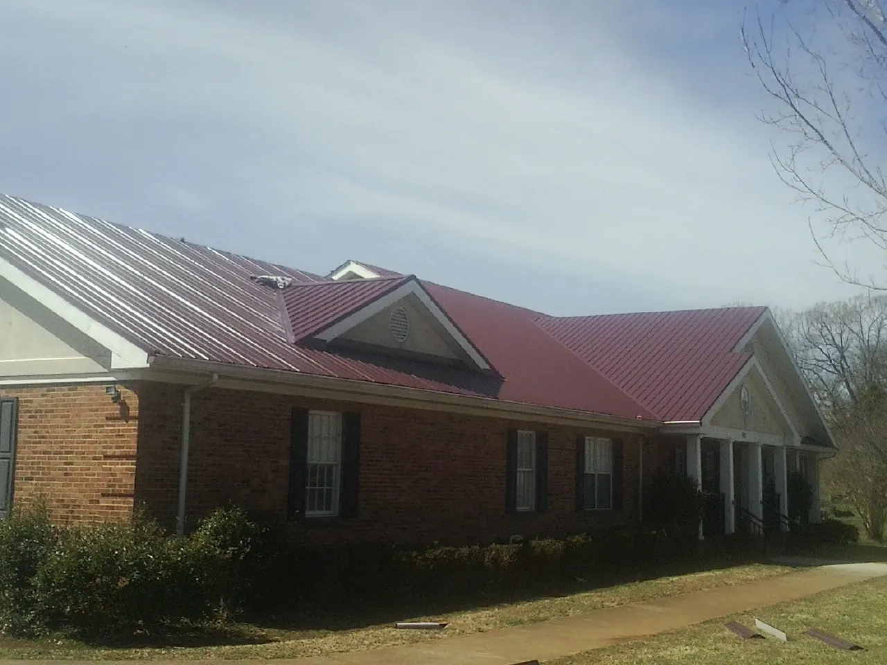 Red metal roof with gabled entries on a long brick building, from a Hail Damage Roof Repair job in Gnadenhutten
