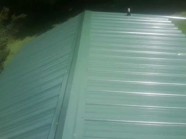 New green metal panels meeting at the ridge of a roof — Flat Roof Repair work by our crew in Gnadenhutten