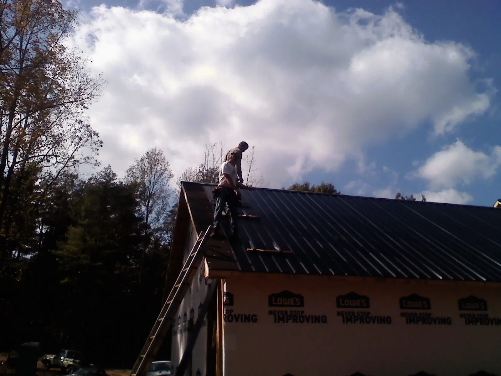 Roofer fastening dark metal panels high against a cloudy sky, from a Roof Inspection job in Gnadenhutten