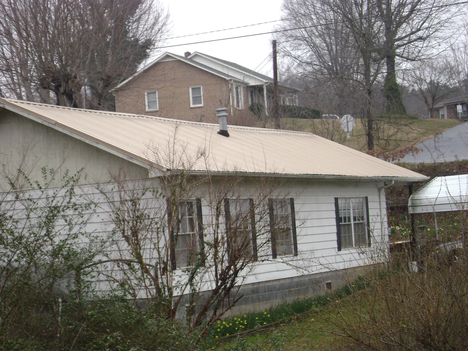 Tan metal roof on a white sided house set into a hillside — Commercial Roofing by Roofing Brothers in Gnadenhutten